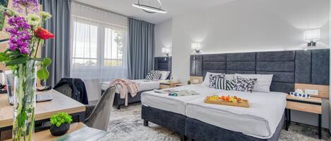 Habitación de hotel moderna con una cama grande, un escritorio con una computadora portátil, un florero con flores y vistas al exterior.