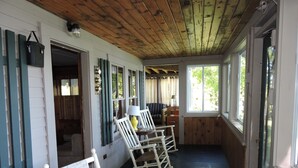 A cozy room with wooden floors, white walls, and a wooden ceiling. There are two rocking chairs, a table with a lamp, and a window with curtains. - Quintessential Winnipesaukee Lake Cottage Sleeps 8 with Views and Dock (Moultonborough)