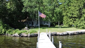 A wooden dock extending into a calm body of water, with an American flag at the end. - Quintessential Winnipesaukee Lake Cottage Sleeps 8 with Views and Dock (Moultonborough)