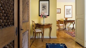 A room with a wooden floor, a dining table with chairs, a vase with flowers, and framed pictures on the wall.