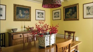 A dining area with a wooden table, chairs, a decorative vase with red flowers, and framed artwork on the wall.