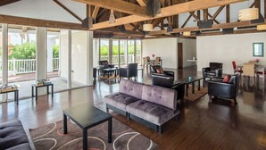 A spacious living area with a high ceiling, wooden beams, and a large window overlooking a balcony.