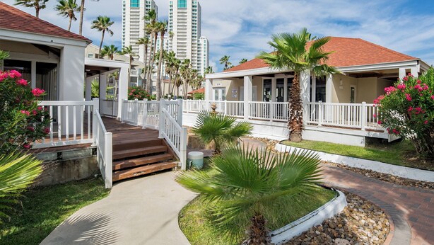 A resort with a covered walkway, palm trees, and a view of tall buildings in the background.