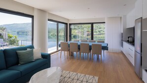 A modern living room with a sofa, dining table, and chairs. There is a large window offering a view of a lake and hills. - Lajinha do Ave (Braga)