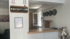 A reception area with a wooden reception desk, a 'RECEPTION' sign, a menu board, and a wall clock. - Aristo2 Butik Otel (Didim)