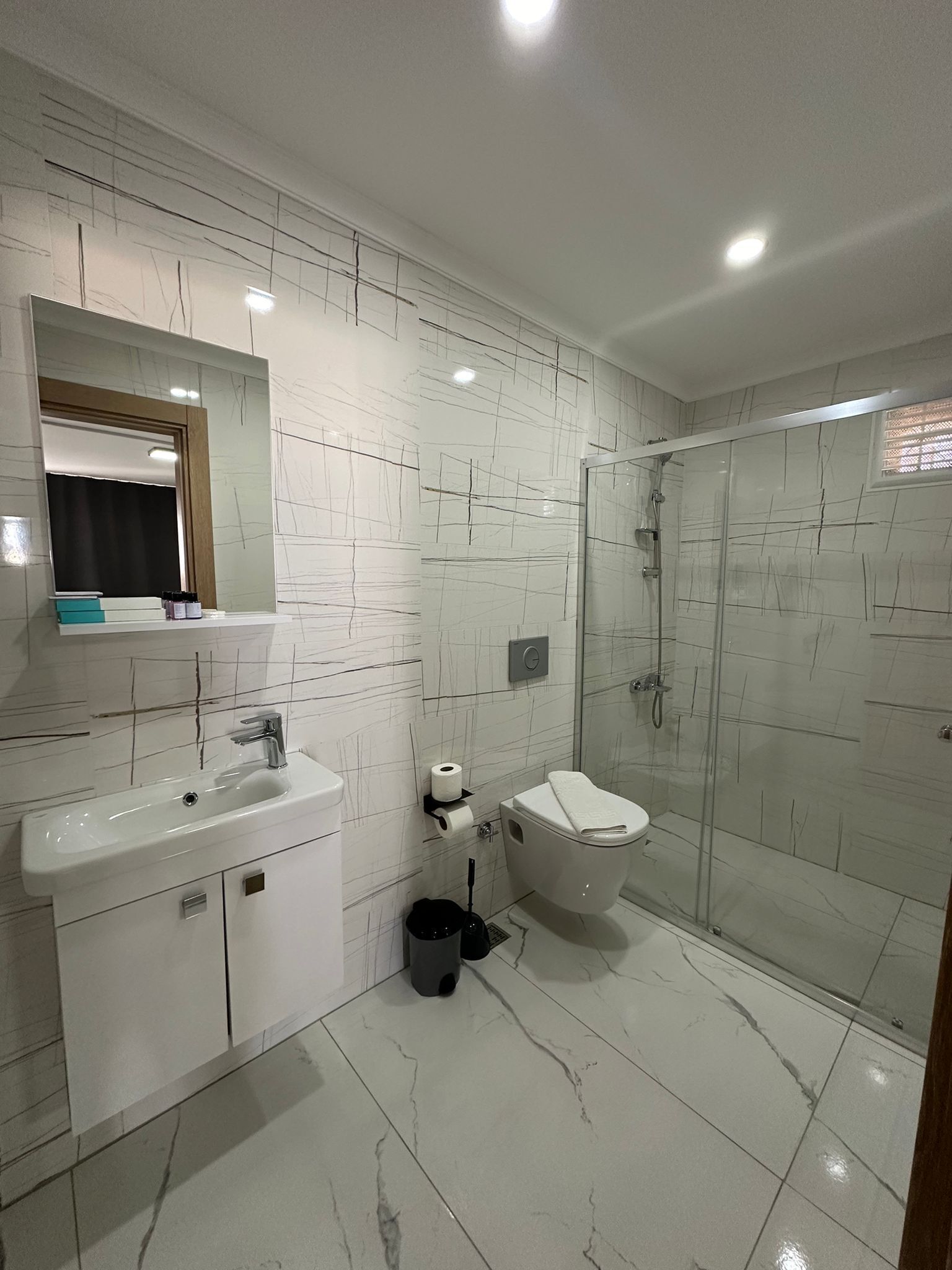 Une salle de bain moderne avec un lavabo en marbre blanc, des toilettes et une douche à parois de verre.