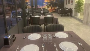 A restaurant with tables set for dining, a mural of a sunset, and a view of the street outside. - Aristo2 Butik Otel (Didim)