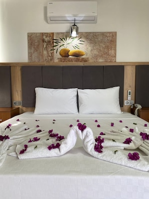 Habitación de hotel con cama, almohadas blancas, aire acondicionado de pared, un adorno en la pared y un teléfono junto a la cama.
