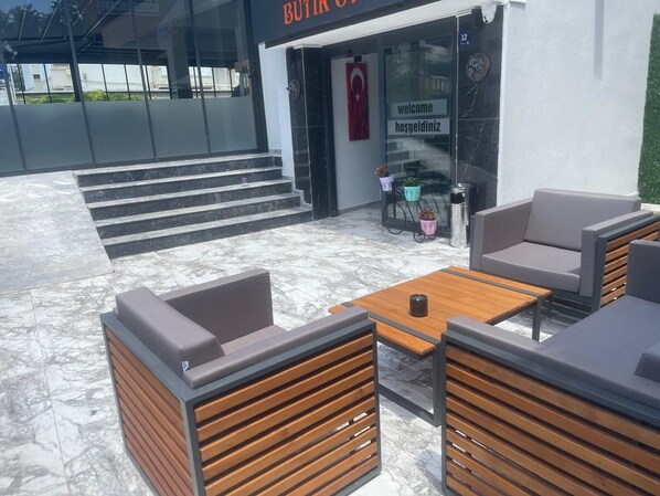 Un área de estar al aire libre con muebles modernos, una escalera que conduce a la entrada de un edificio y un cartel de bienvenida en un idioma extranjero.