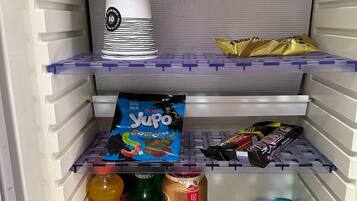 A refrigerator stocked with various food items including a bottle of Fanta, a green bottle, a can of salt, a box of Yupo, and a pack of chocolate bars.