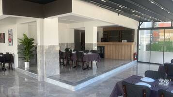 A modern hotel lobby with marble flooring, a reception desk, and a dining area with tables and chairs.