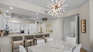 A modern kitchen with white cabinetry, a central island, and a dining area with a glass table and white chairs.