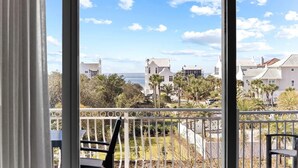A view from a balcony with a railing, overlooking a coastal area with buildings and palm trees.