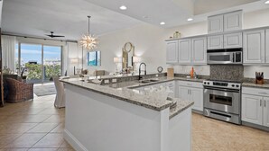 A modern kitchen with white cabinetry, a granite countertop, stainless steel appliances, and a large island.
