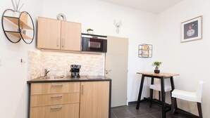 A compact kitchen with wooden cabinets, a built-in oven, a coffee maker, and a small dining table with a chair. - Studio Quiet Downtown Rieumes (Rieumes)
