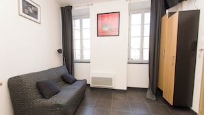 A room with a patterned sofa, a wardrobe, a radiator, and a window with curtains. - Studio Quiet Downtown Rieumes (Rieumes)