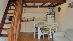 A cozy living room with a wooden staircase, a dining area, and a kitchen.