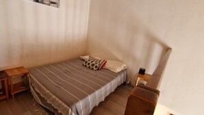 A small, neatly arranged bedroom with a single bed, a wooden nightstand, a small table, and a chair.