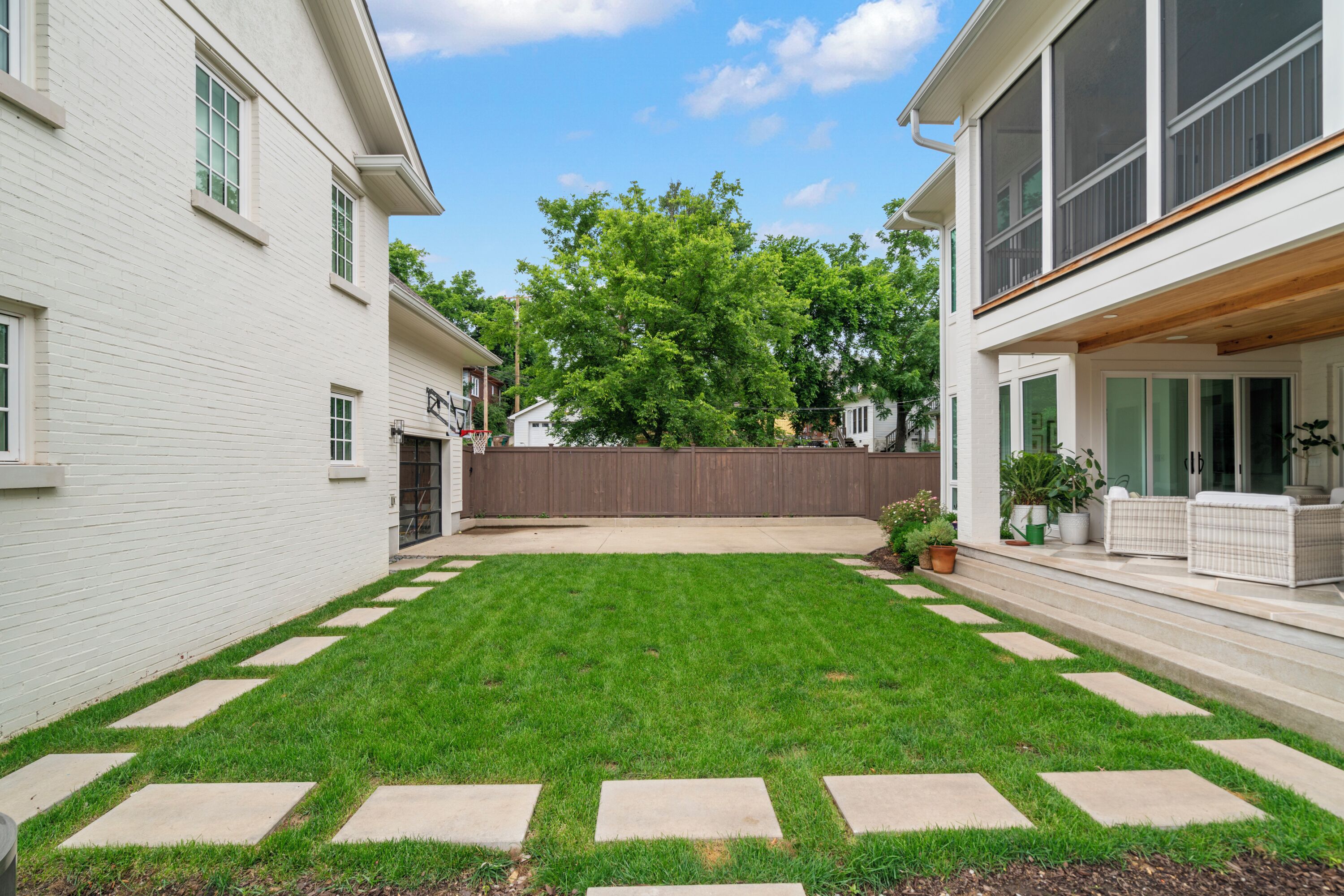 A residential backyard with a well-maintained lawn, a wooden deck, and a white fence.