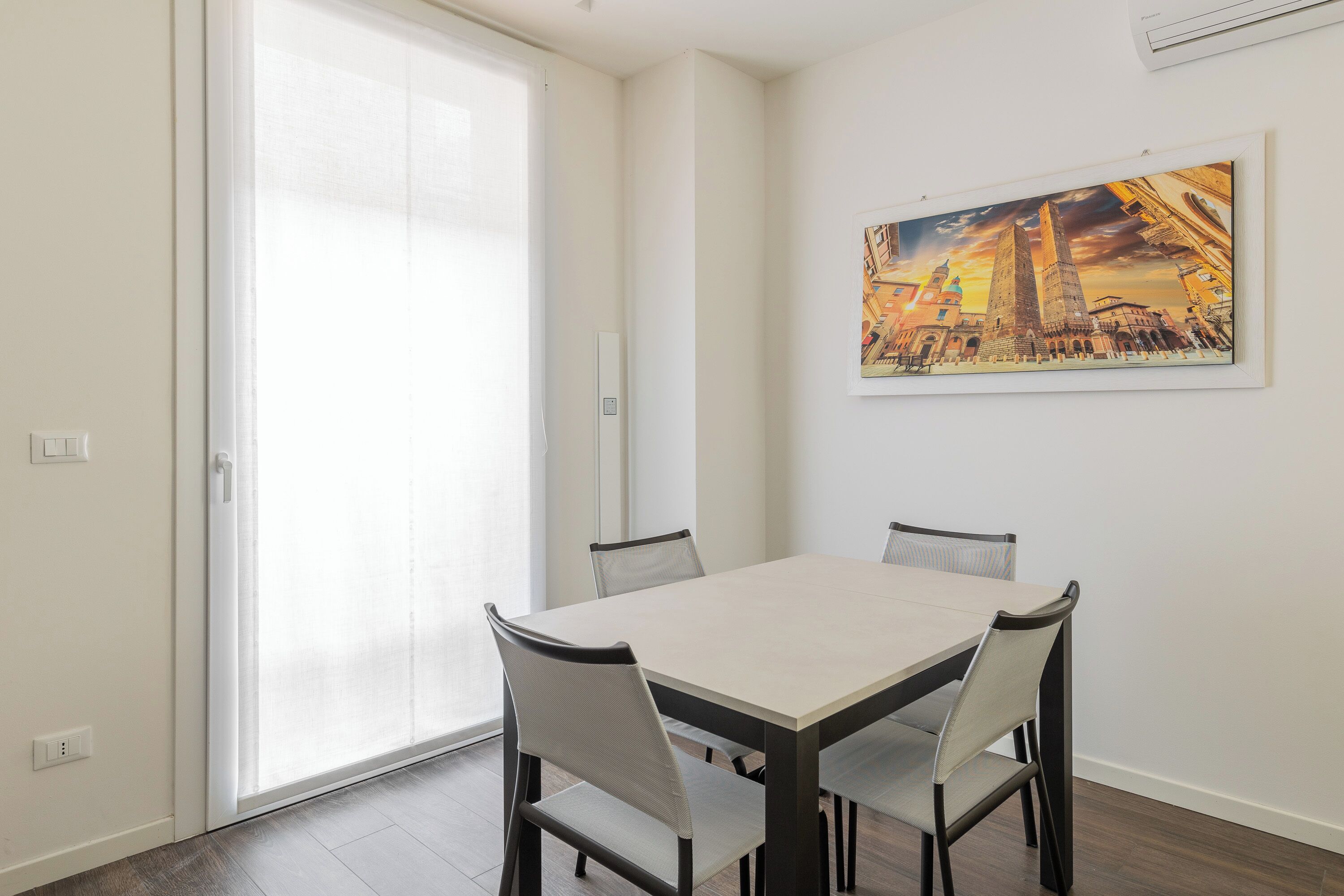 A dining area with a table and chairs, a painting on the wall, and a sliding glass door.