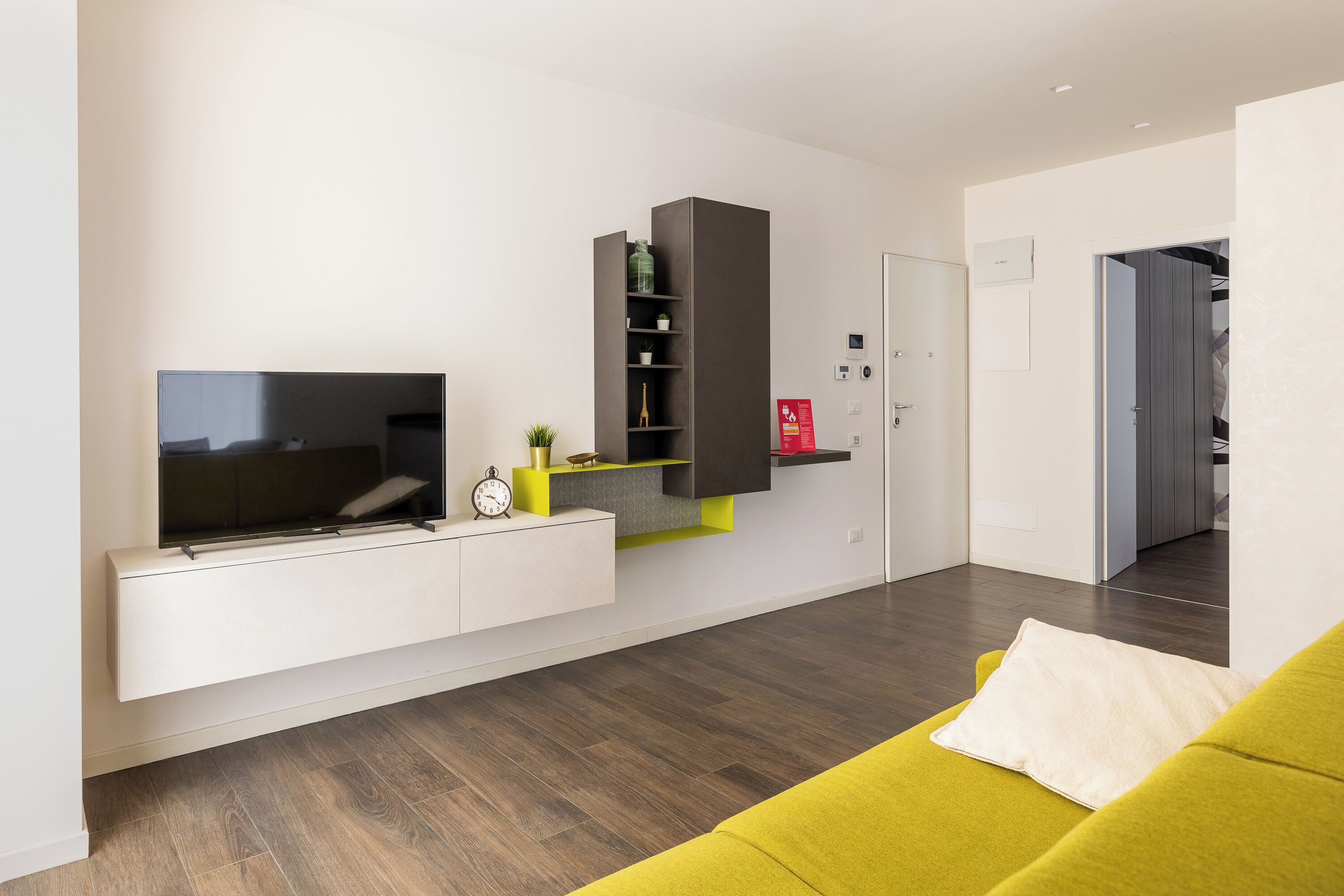 Een moderne woonkamer met een flatscreen televisie, een bank en inbouwkasten met decoratieve objecten.