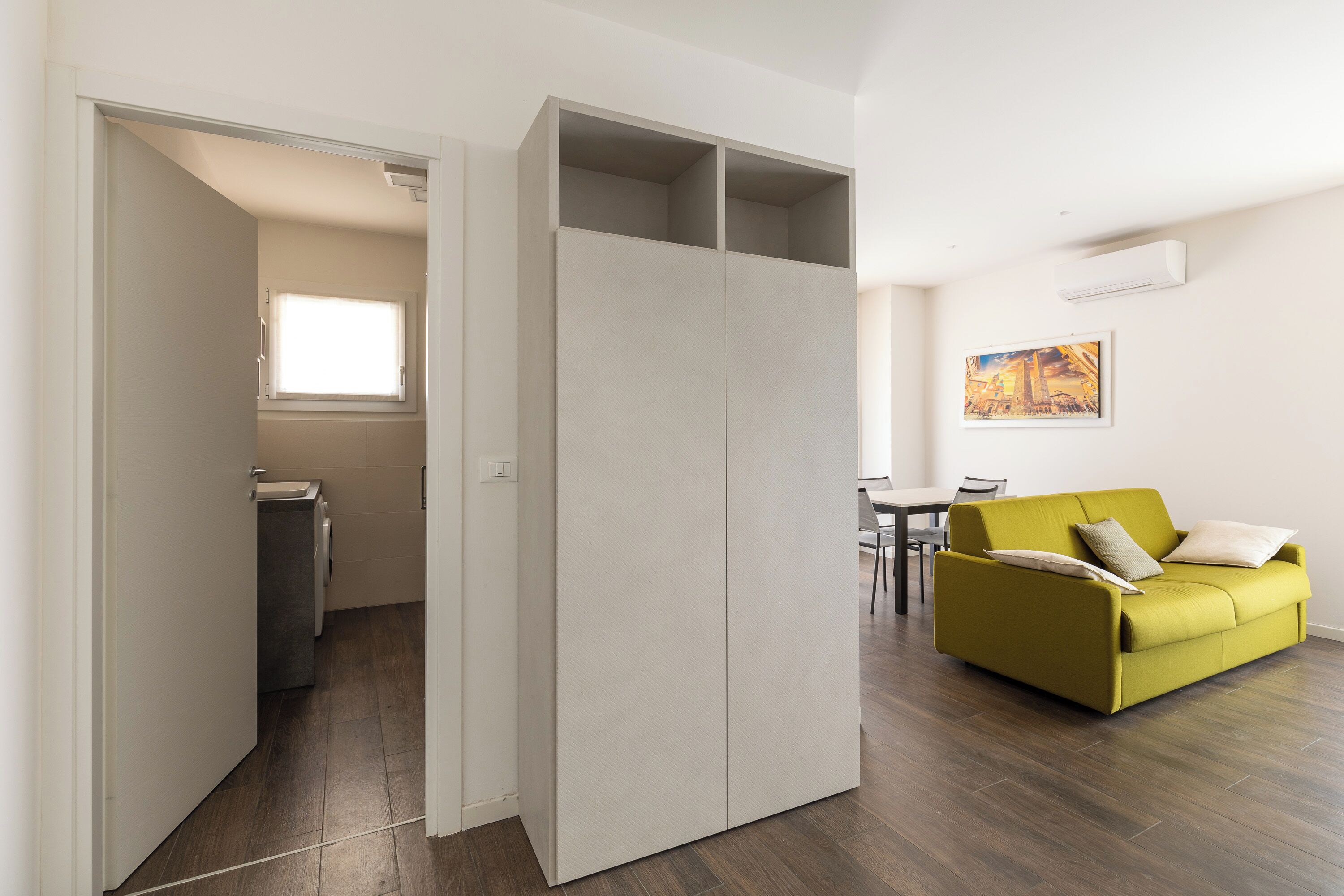 A modern living room with a yellow sofa, a dining table, and a large wardrobe.