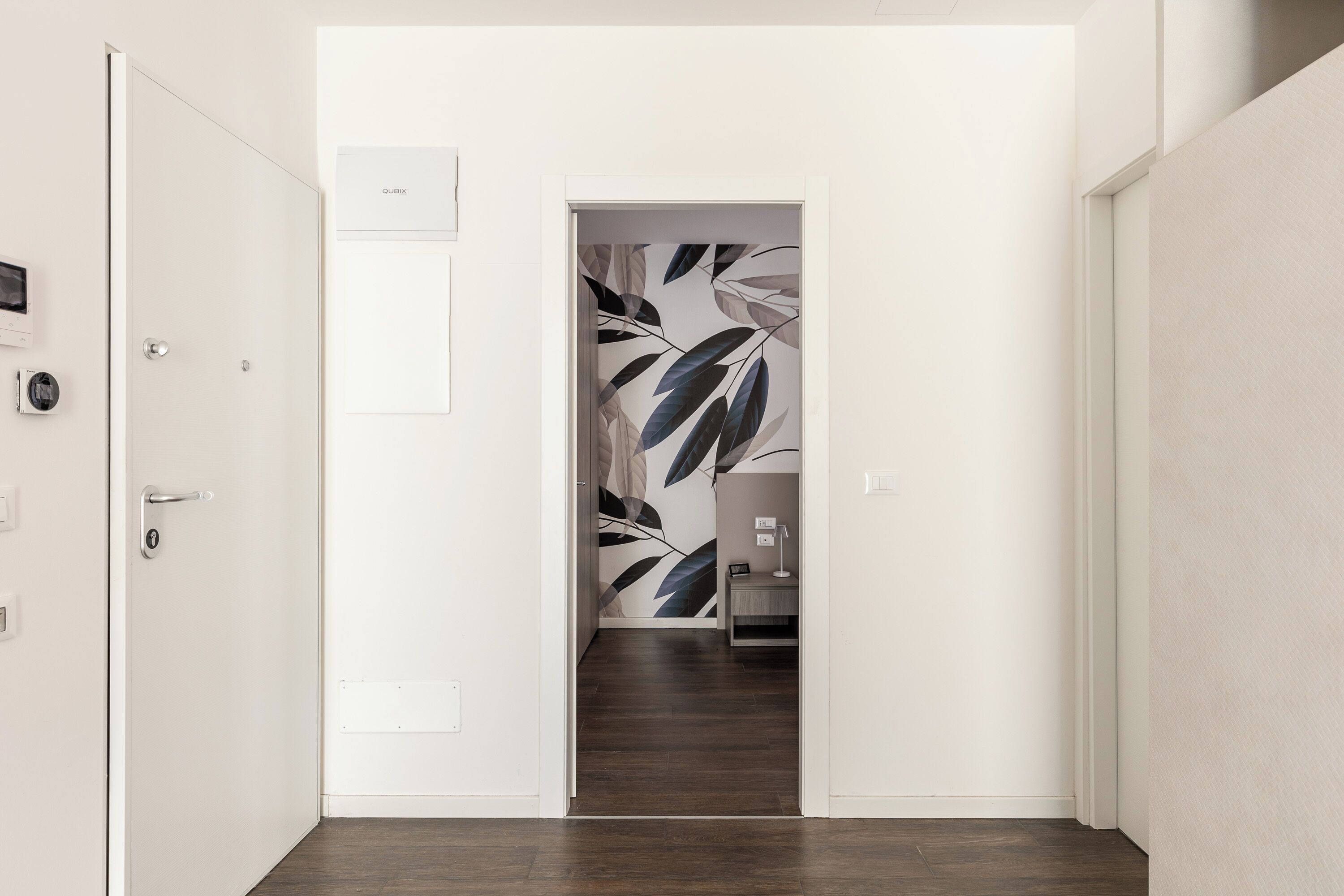 A hallway with a door leading to a room with a leaf-patterned wall.