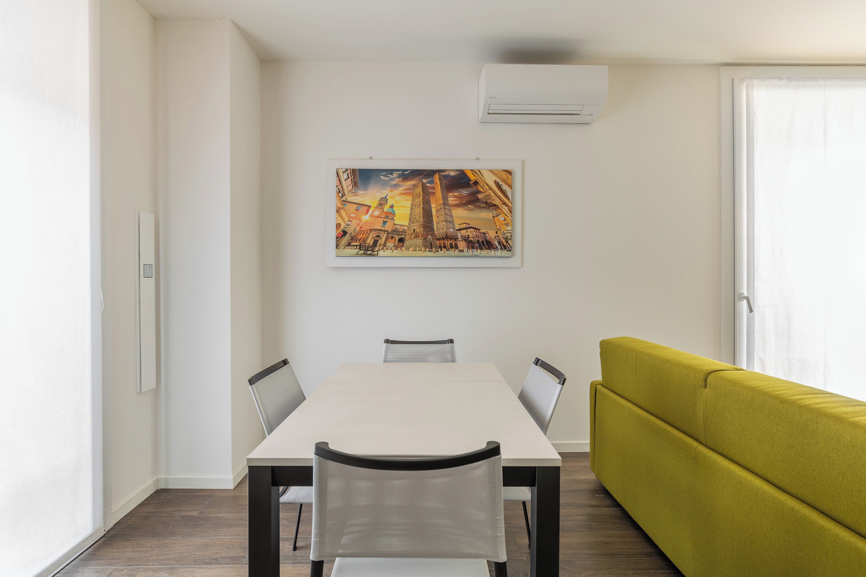 A dining area with a table and chairs, a yellow sofa, and a painting on the wall.