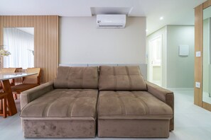 A modern living room with a beige sectional sofa, a dining table with chairs, and a large window with blinds. - Las Vegas  (Bombinhas)
