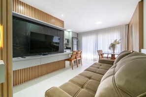 Una sala de estar moderna con un televisor de pantalla plana grande, paneles de madera, un sofá beige y un comedor con sillas y una mesa.