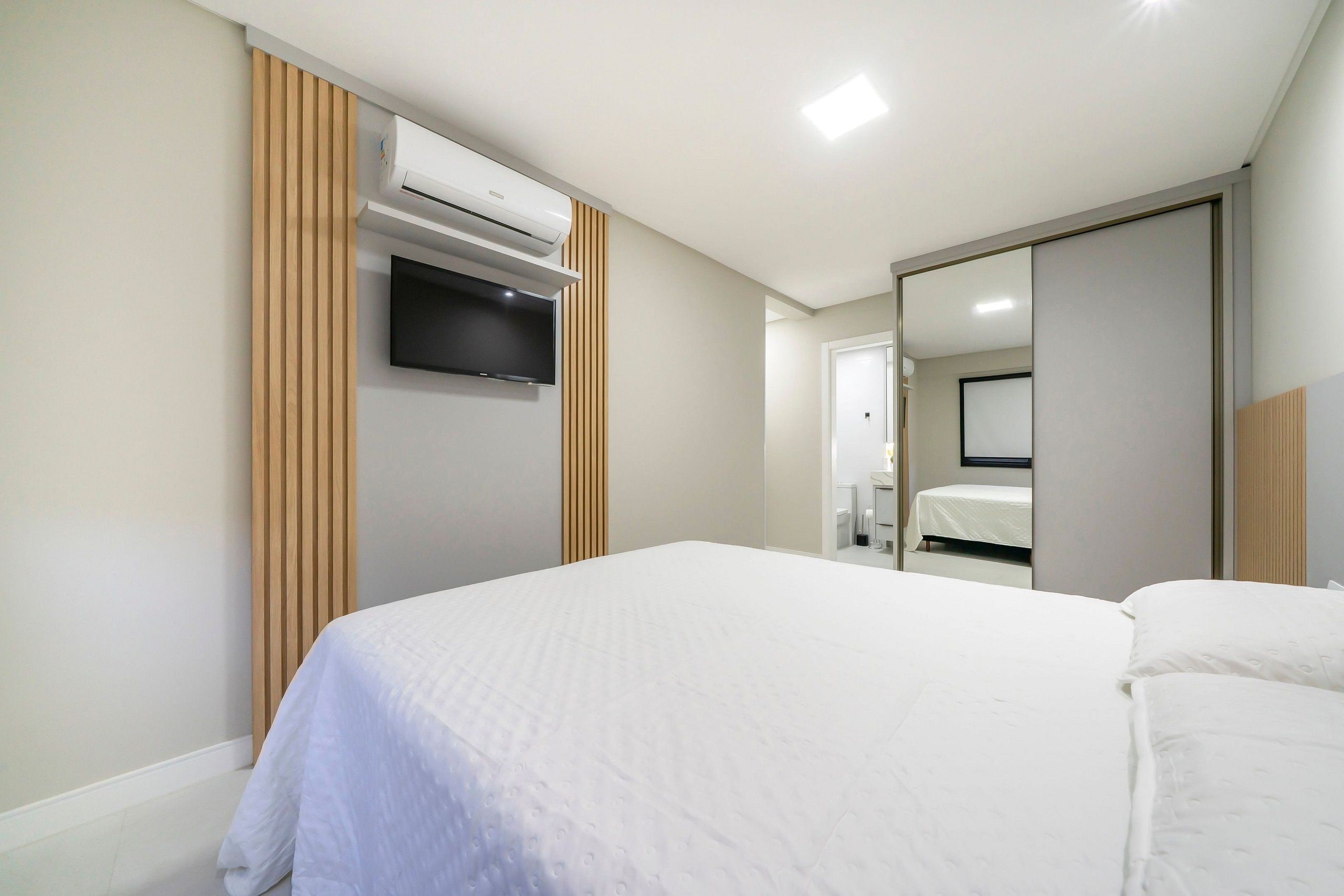 A hotel room with a bed, a flat-screen TV mounted on the wall, an air conditioning unit, and a sliding door leading to a bathroom.