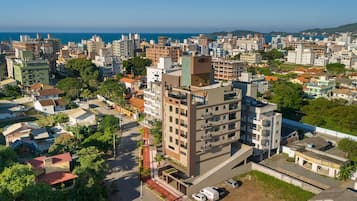 A high-rise building with multiple floors, surrounded by other residential buildings, a road with vehicles, and a view of the sea in the background.