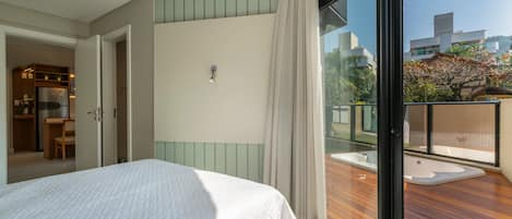 Un dormitorio con cama, puerta corrediza a un baño y vista a una terraza de madera con hidromasaje.