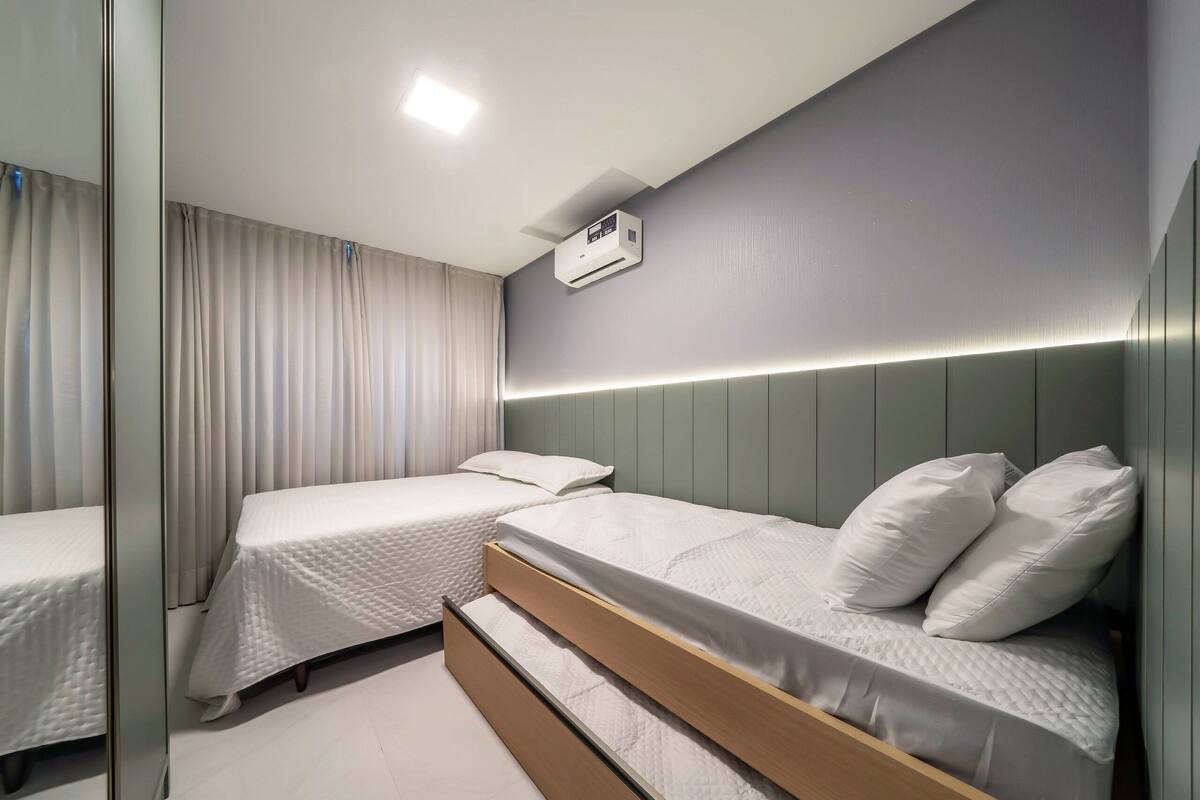Une chambre d’hôtel moderne équipée de deux lits simples, d’une banquette intégrée, d’un climatiseur fixé au plafond et d’une table de chevet.