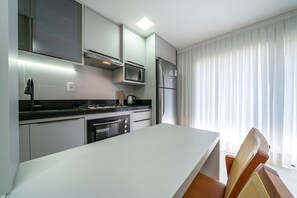 A modern kitchen with a white countertop, stainless steel appliances, and a dining area with a wooden chair. - Las Vegas  (Bombinhas)
