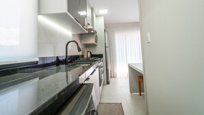 Una cocina moderna con encimera de granito, electrodomésticos de acero inoxidable y una ventana con cortinas translúcidas.