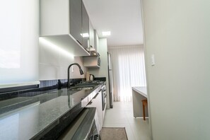 Una cocina moderna con encimera de granito, electrodomésticos de acero inoxidable y una ventana con cortinas translúcidas.