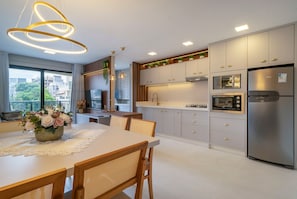 A modern kitchen with stainless steel appliances, a dining area with a lace tablecloth, and a view of the city through large windows. - Las Vegas (Bombinhas)