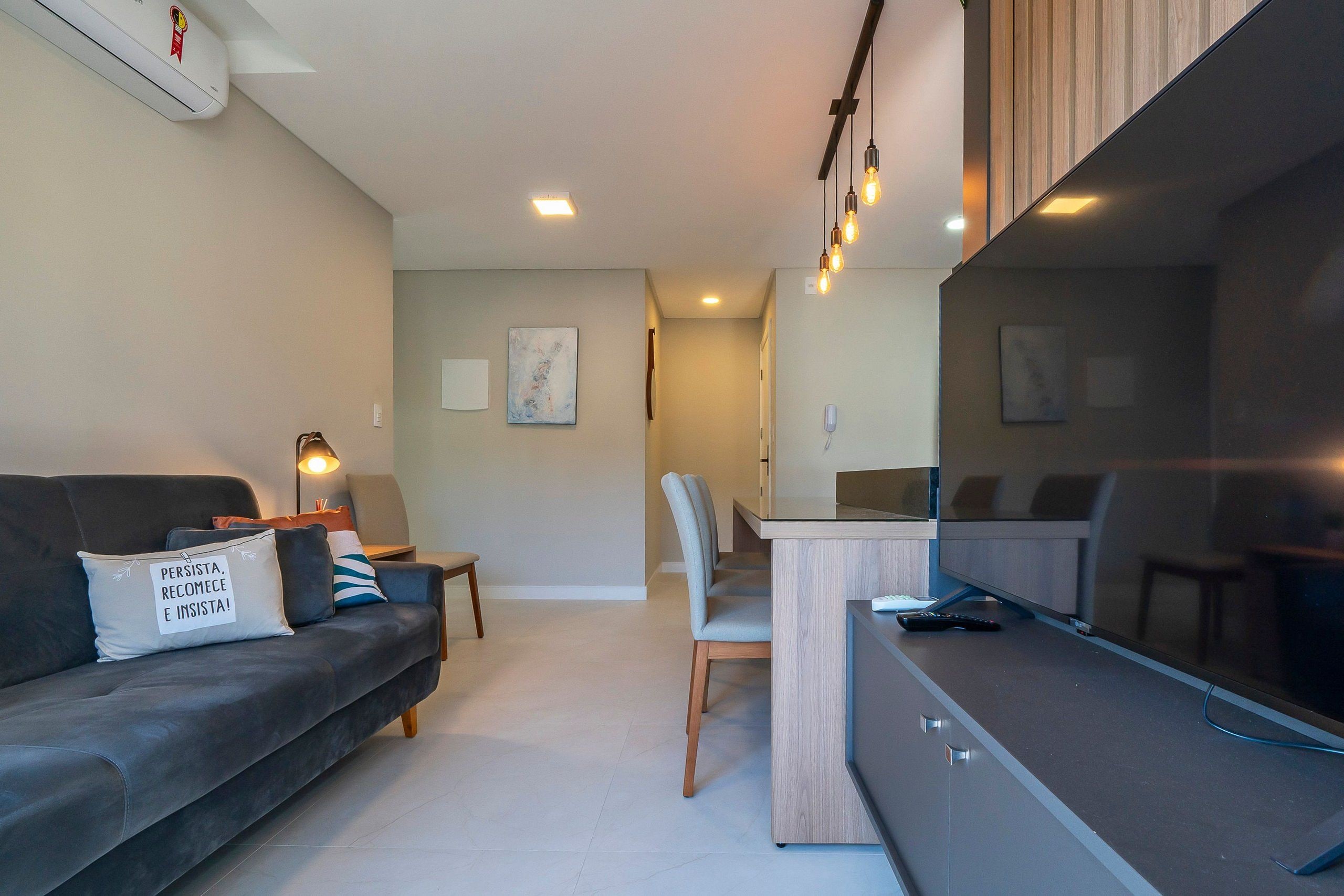 Un salon moderne avec un canapé, un coin repas comprenant une table et des chaises, et un grand téléviseur.