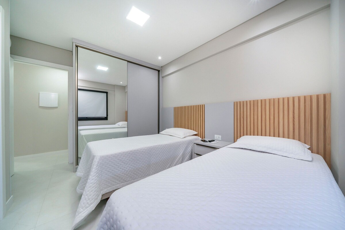 Una habitación de hotel moderna con dos camas individuales, un cabecero de madera, una mesita de noche pequeña y un espejo.