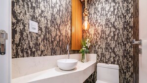 Un baño con lavamanos blanco, tocador de madera y retrete.
