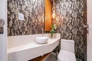 Un baño con lavamanos blanco, tocador de madera y retrete.
