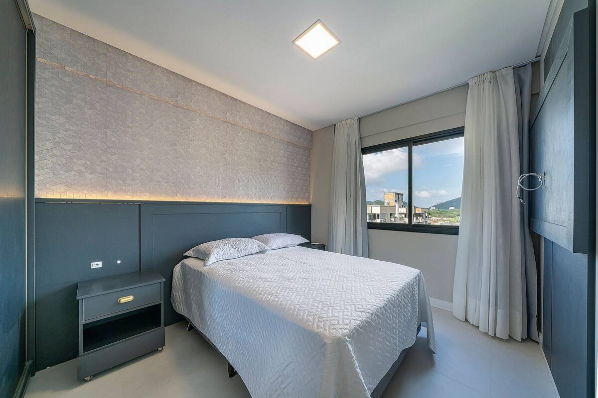 Une chambre moderne avec un grand lit, une table de chevet, une étagère intégrée et une fenêtre avec des rideaux.
