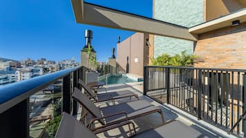 Terraço no telhado com piscina, espreguiçadeiras e vista para a paisagem urbana.