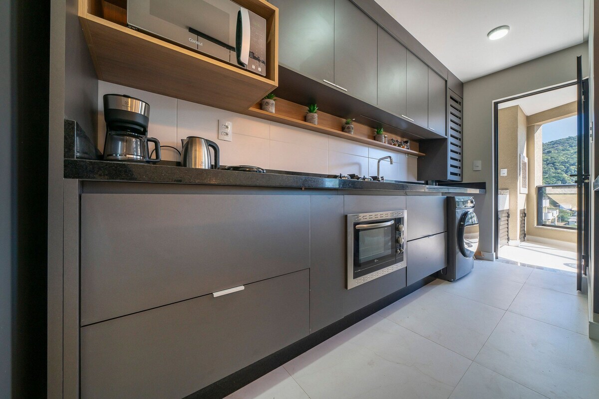 Una cocina moderna con electrodomésticos integrados, estantes de madera y vistas al exterior.