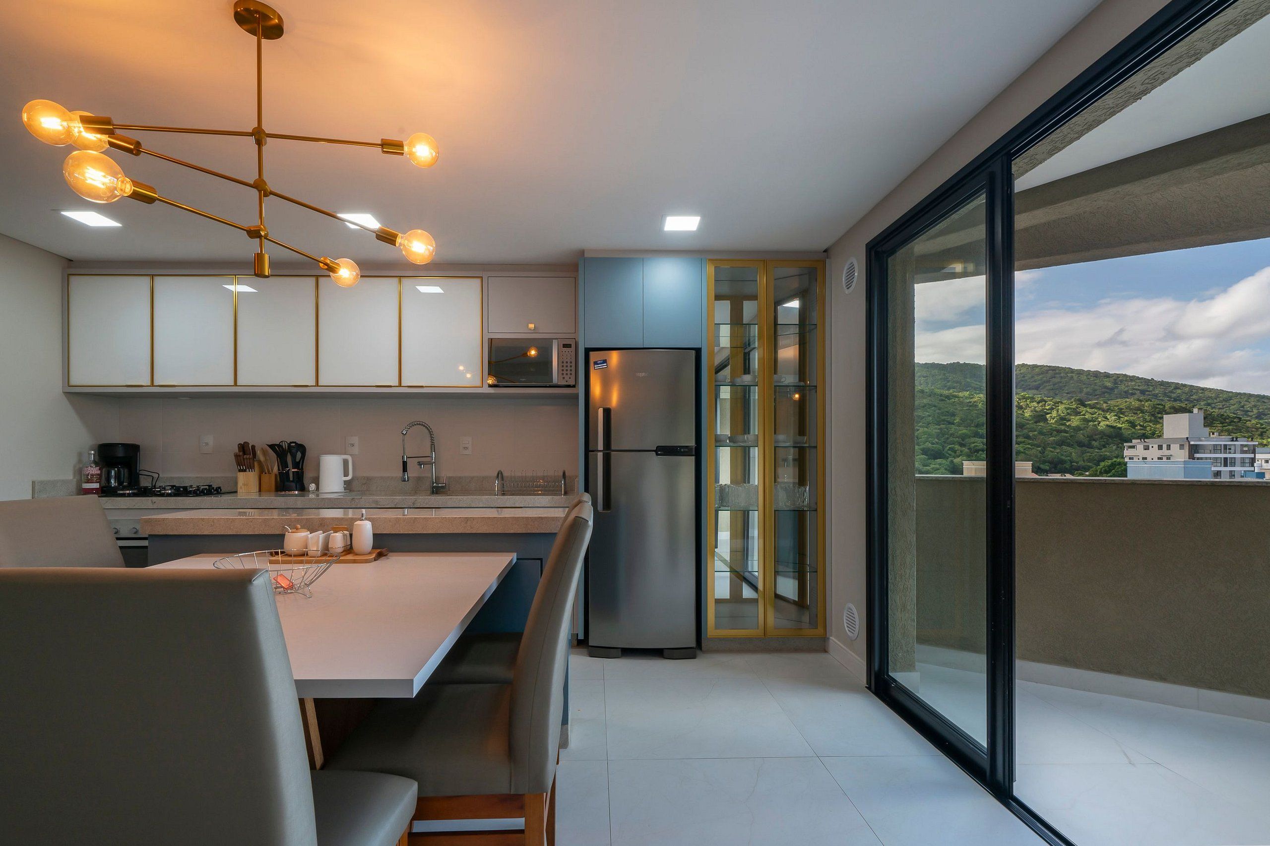 A modern kitchen with a dining area, a stainless steel refrigerator, and a view of a cityscape through large sliding glass doors.