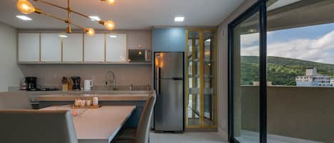 A modern kitchen with a dining area, a stainless steel refrigerator, and a view of a cityscape through large sliding glass doors.