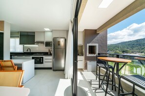 A modern kitchen with a refrigerator, microwave, and stove. There is a balcony with a table and chairs. - Las Vegas (Bombinhas)
