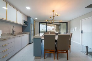 A modern kitchen with a dining area, featuring a built-in microwave, stainless steel appliances, and a contemporary chandelier. - Las Vegas  (Bombinhas)