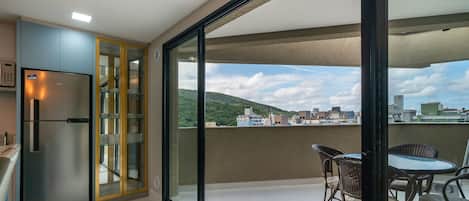 Un balcón con zona de comedor, refrigerador y vista a la ciudad.